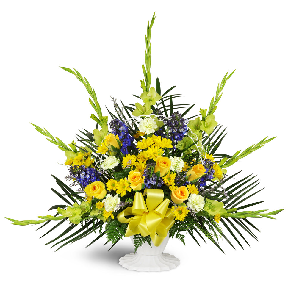 Heaven’s Promise Sympathy Tribute™ - Deluxe. Features a classic white basket blooming with blue delphinium, yellow daisies, and gladiolus—a yellow bow adds the finishing touch.