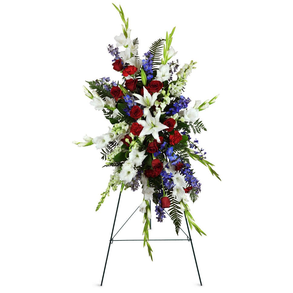Gentle Repose Lily Spray™. Large white lilies, white gladiolus, and classic red roses are tastefully arranged for display at the funeral or service.