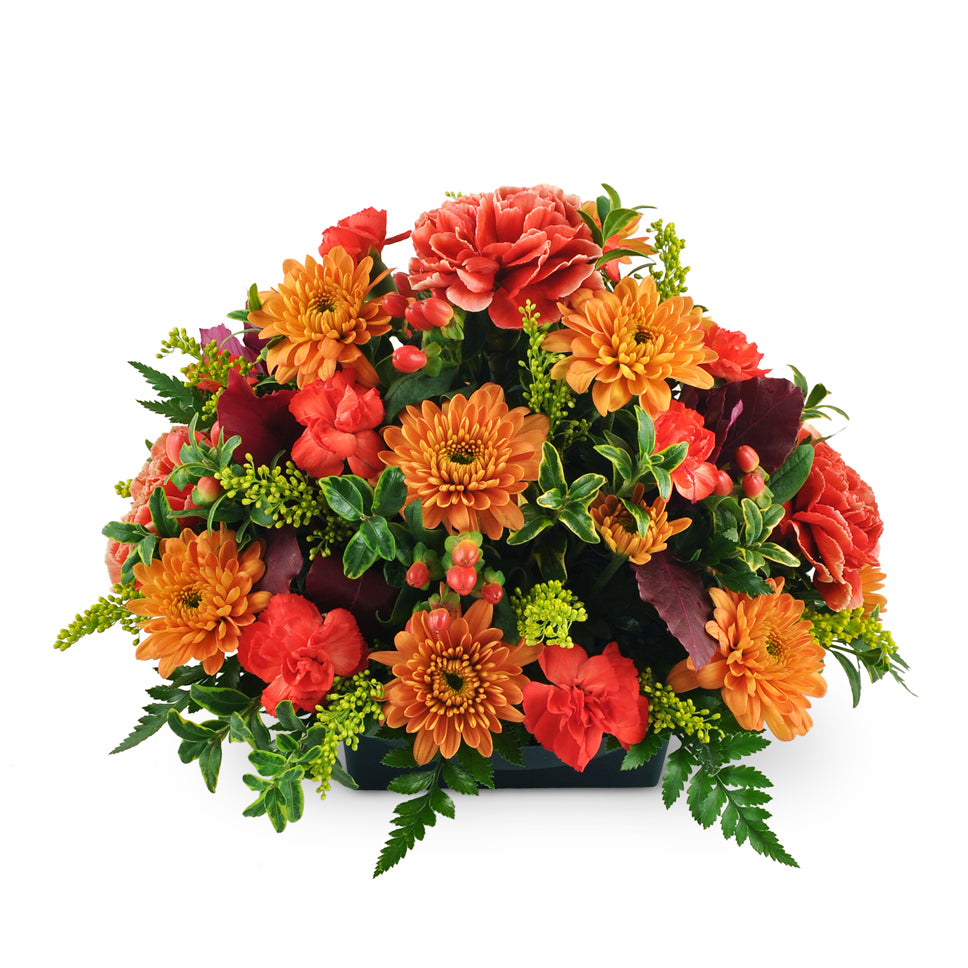 Heart of the Home Centerpiece™. Carnations, mini carnations, and chrysanthemums are arranged with hypericum berries, solidago, preserved leaves, oregonia, and leatherleaf.