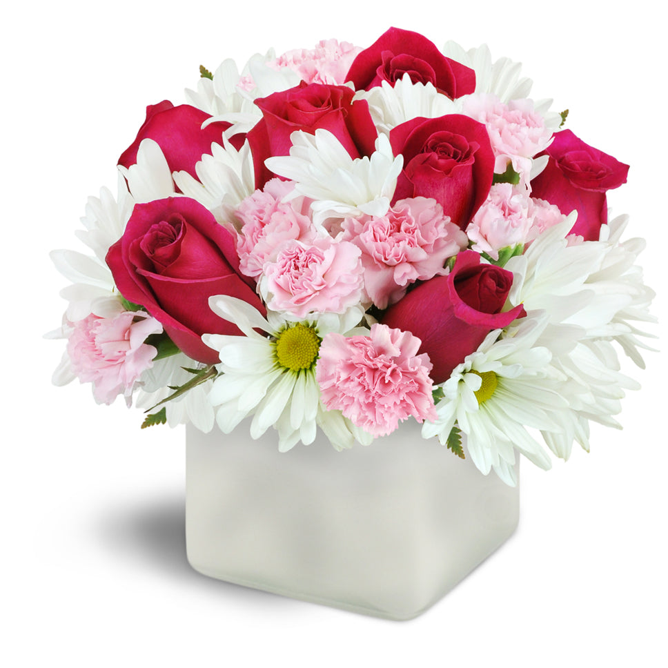 Vibrant Blooms™ - Premium. Hot pink roses are beautifully arranged with soft pink mini carnations and white daisies in a glass cube vase.