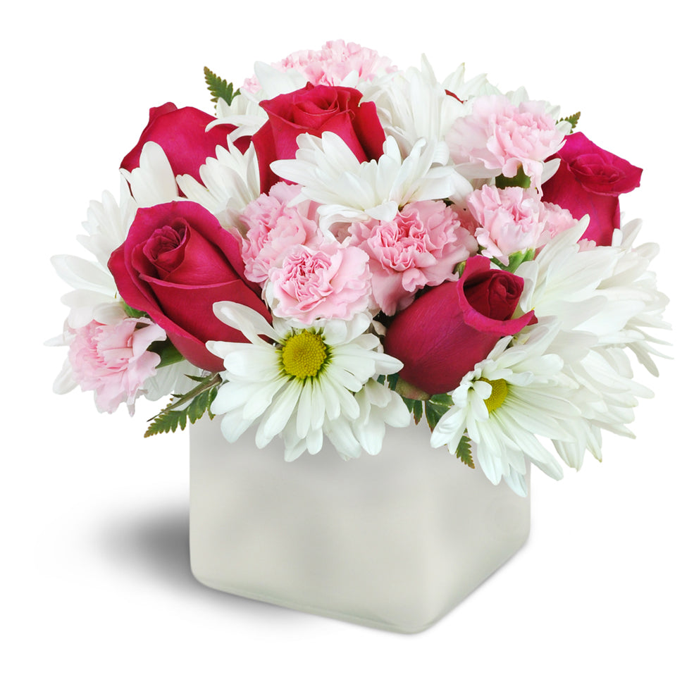 Vibrant Blooms™ - Deluxe. Hot pink roses are beautifully arranged with soft pink mini carnations and white daisies in a glass cube vase.