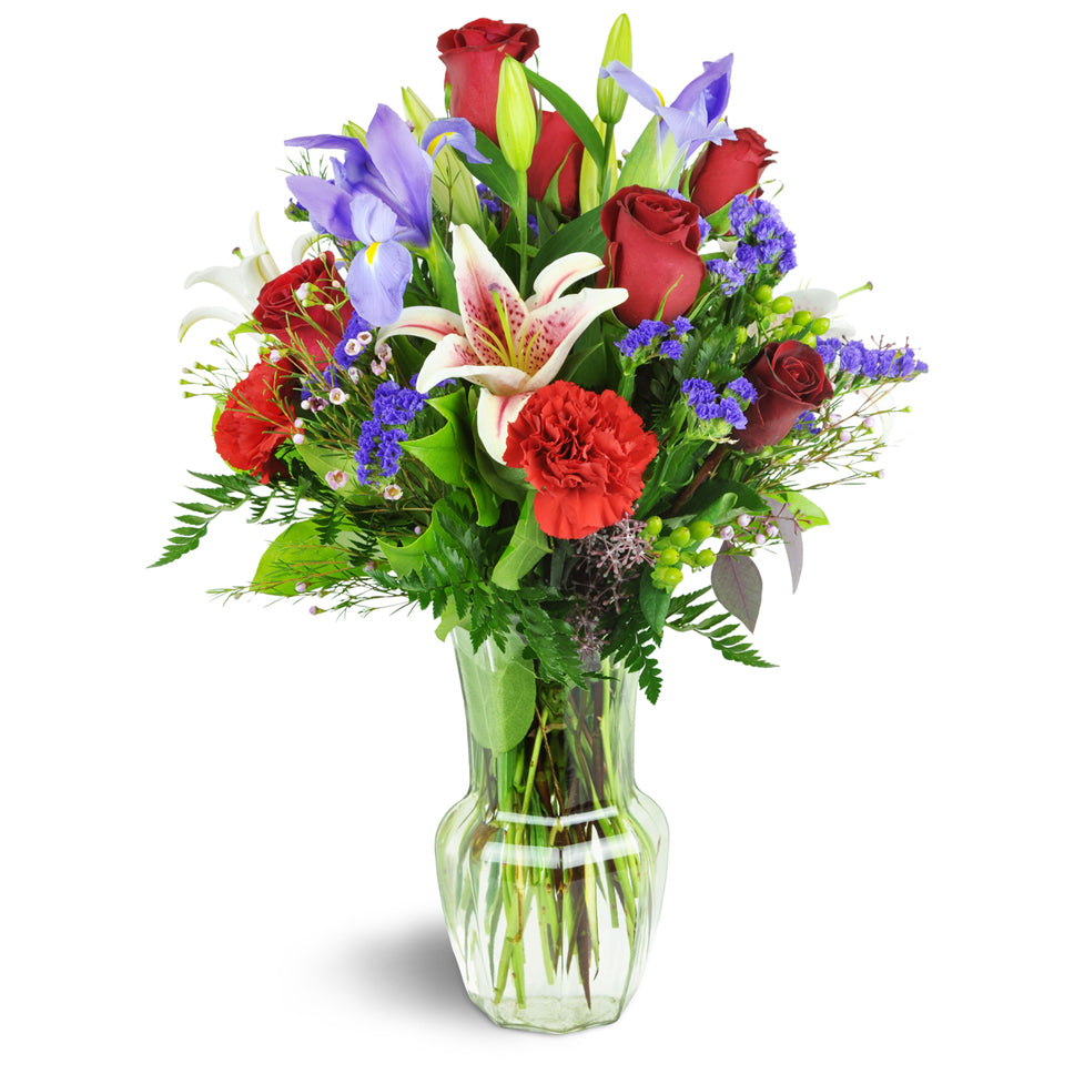 Berry Wonderful. A tall elegant flower arrangement in a clear vase with roses, carnations, Stargazer lilies, irises.