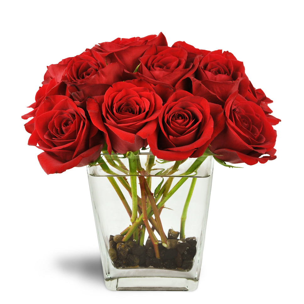 Love's Destiny Bouquet™ - Standard. Large red rose blooms burst from a clear glass vase lined with river rocks.