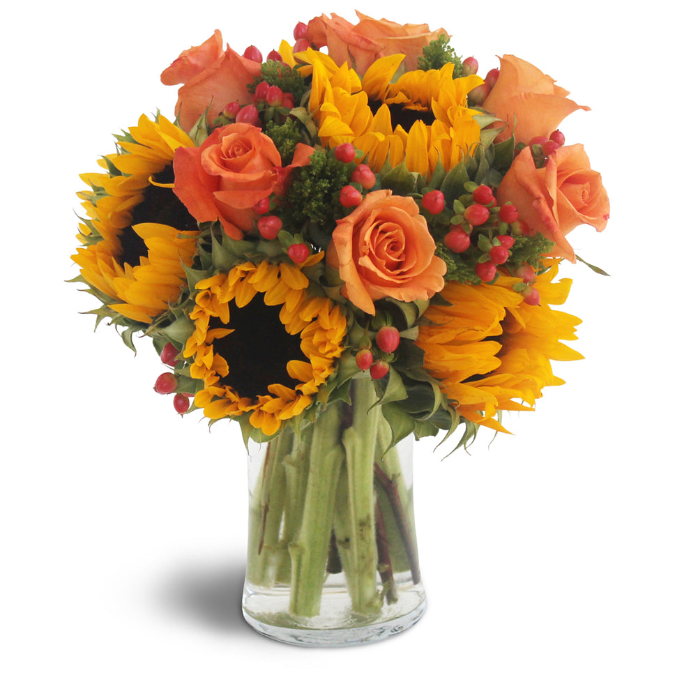 Sweet Harvest Sunflowers™. Sunflowers and coral roses are arranged in a canopy of rustic wheat, hypericum berries, and lush greens.