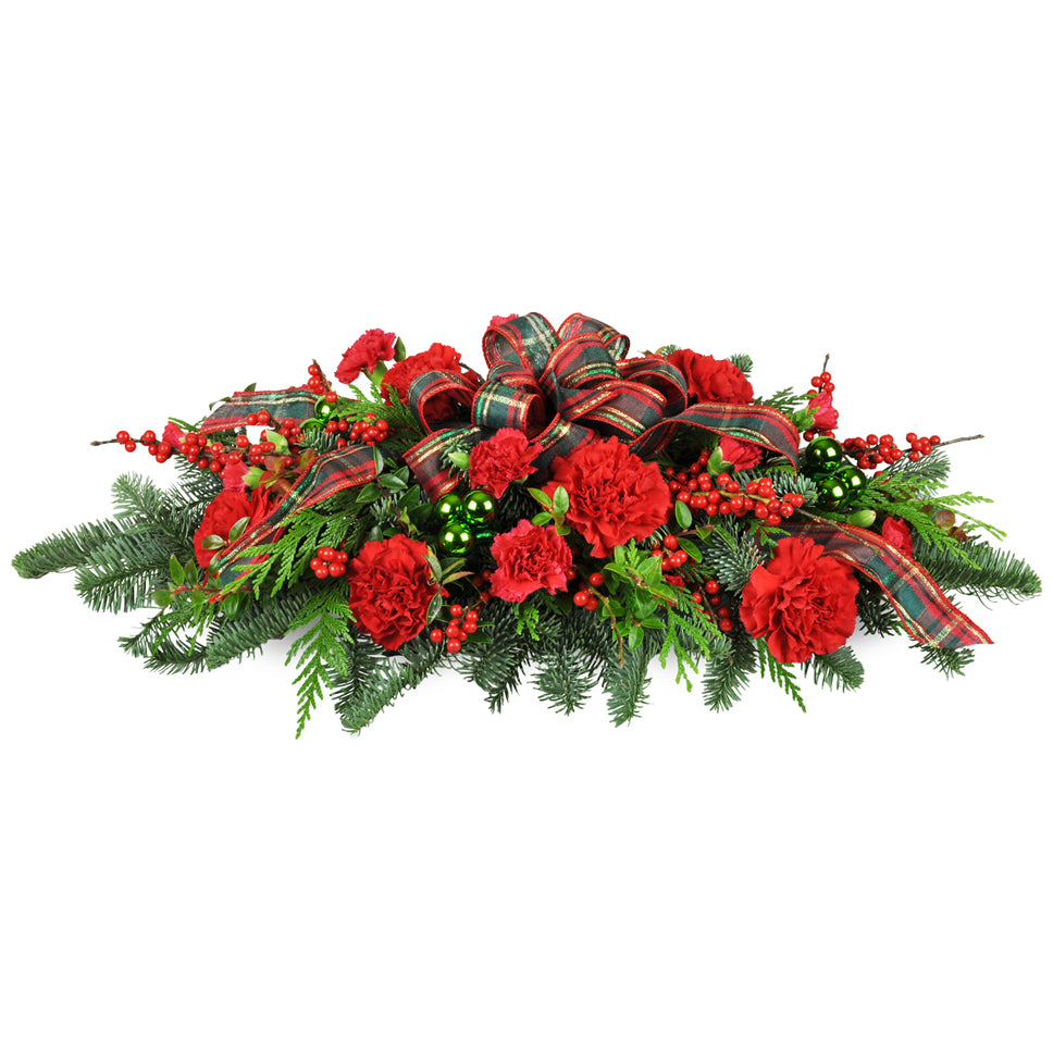 Christmas Traditions Centerpiece™ - Standard. A classic swag is arranged with red carnations, green baubles, pine, cedar, and more.