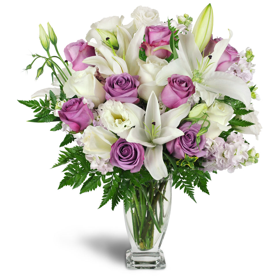 Sweet as Sugar Bouquet™ - Deluxe. White and lavender roses are arranged with Asiatic lilies, stock, lisianthus, and more in an elegant glass vase.