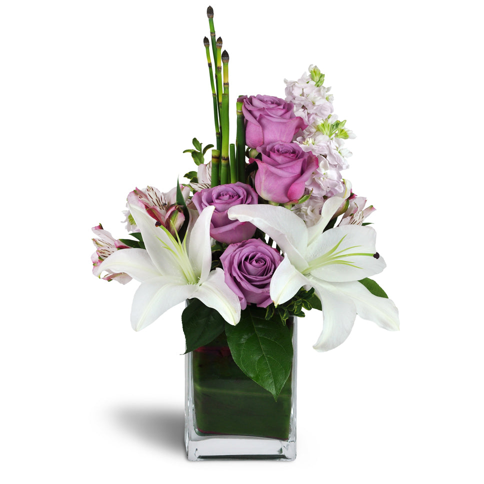 Sweetness and Grace™. White Asiatic lilies and lavender roses are arranged with pink alstroemeria, horsetail, and more.