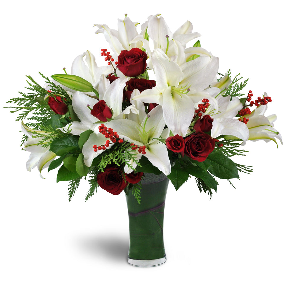 Holiday Kiss™. White Oriental lilies and red roses are arranged with spray roses, ilex berries, cedar, and more in a clear glass vase.