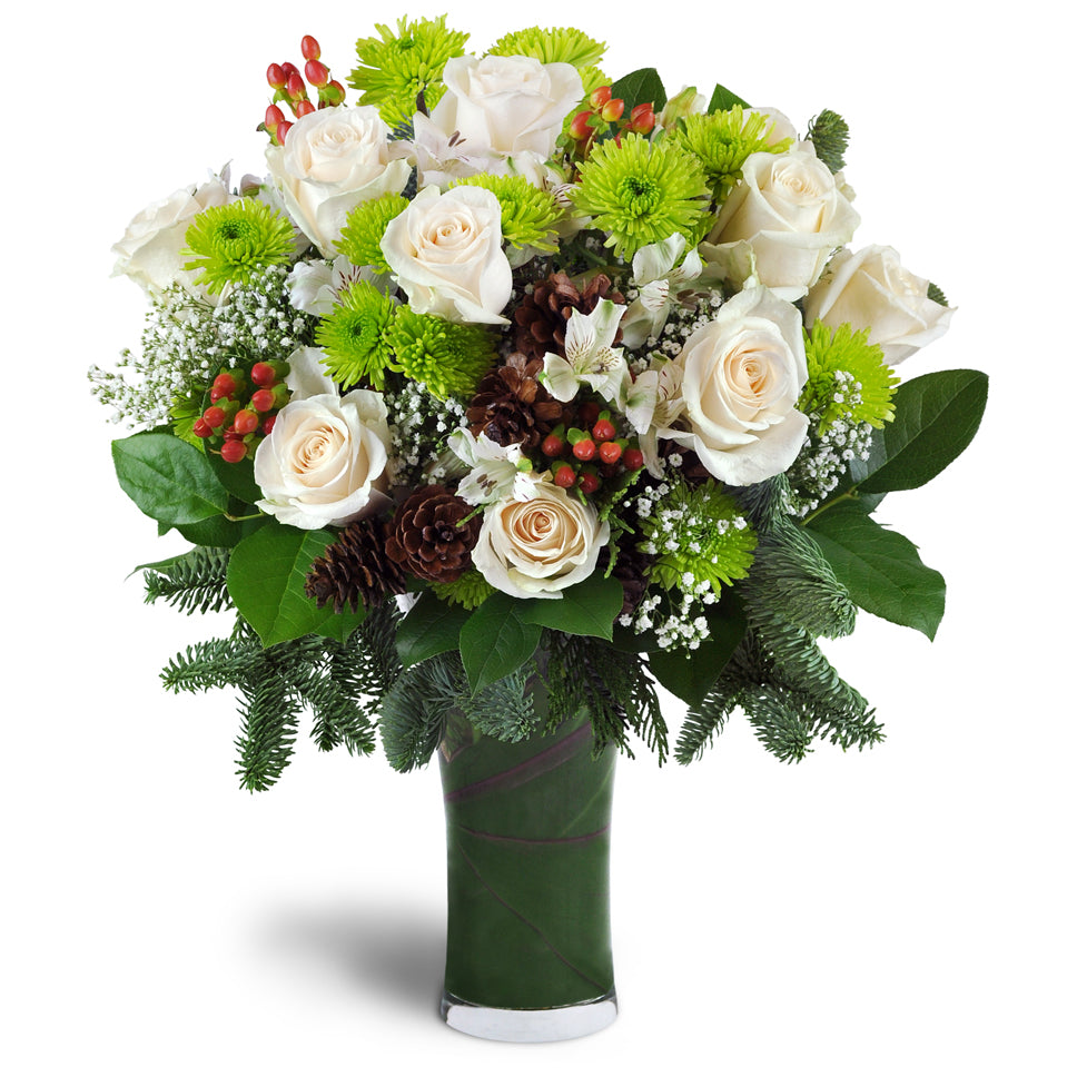 Rustic Holiday™. White roses, green daisy poms, hypericum berries, and more are arranged with pine and pinecones in a clear glass vase.