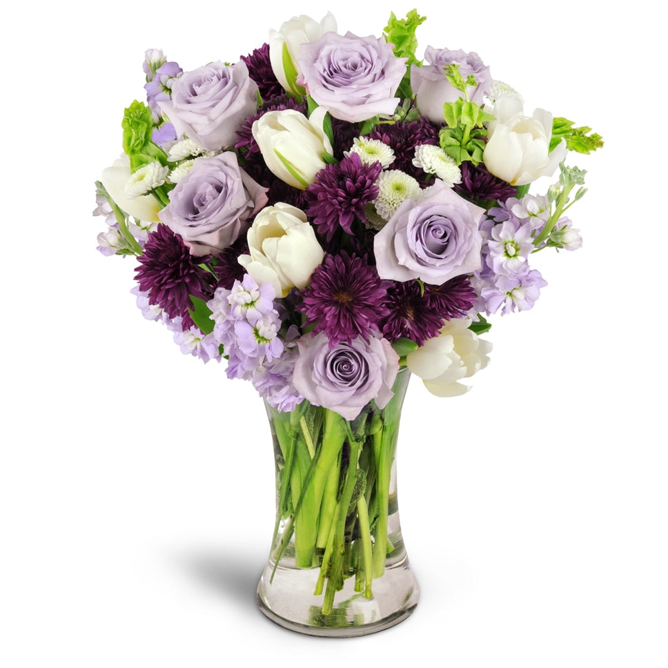 Serene Paradise™ - Premium. White tulips, Bells of Ireland, and more are beautifully arranged in a glass vase. Upgrade to Deluxe or Premium to add gorgeous lavender roses.