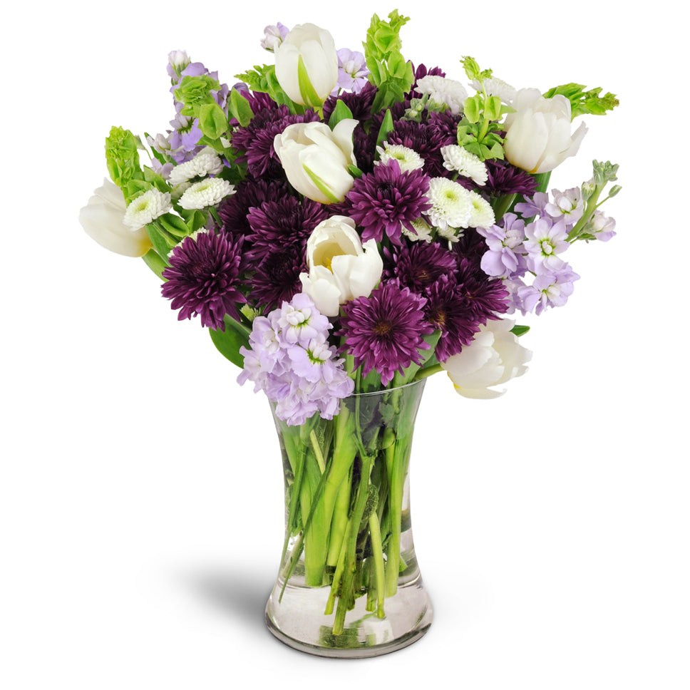 Serene Paradise™. White tulips, Bells of Ireland, and more are beautifully arranged in a glass vase. Upgrade to Deluxe or Premium to add gorgeous lavender roses.