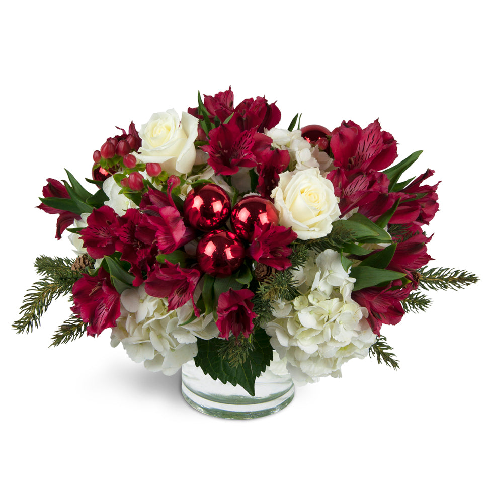Very Merry Bouquet™ - Deluxe. Festive red and white blooms are arranged with holiday greens. Upgrade to Deluxe or Premium to add lovely white roses.