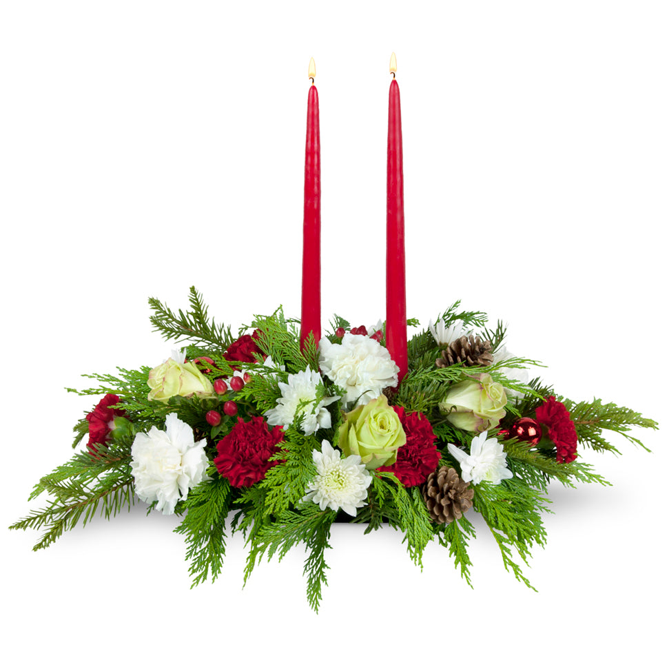 Gather 'Round Centerpiece™ - Deluxe. Red and white blooms are tucked among festive greens and topped with two tapered candles.