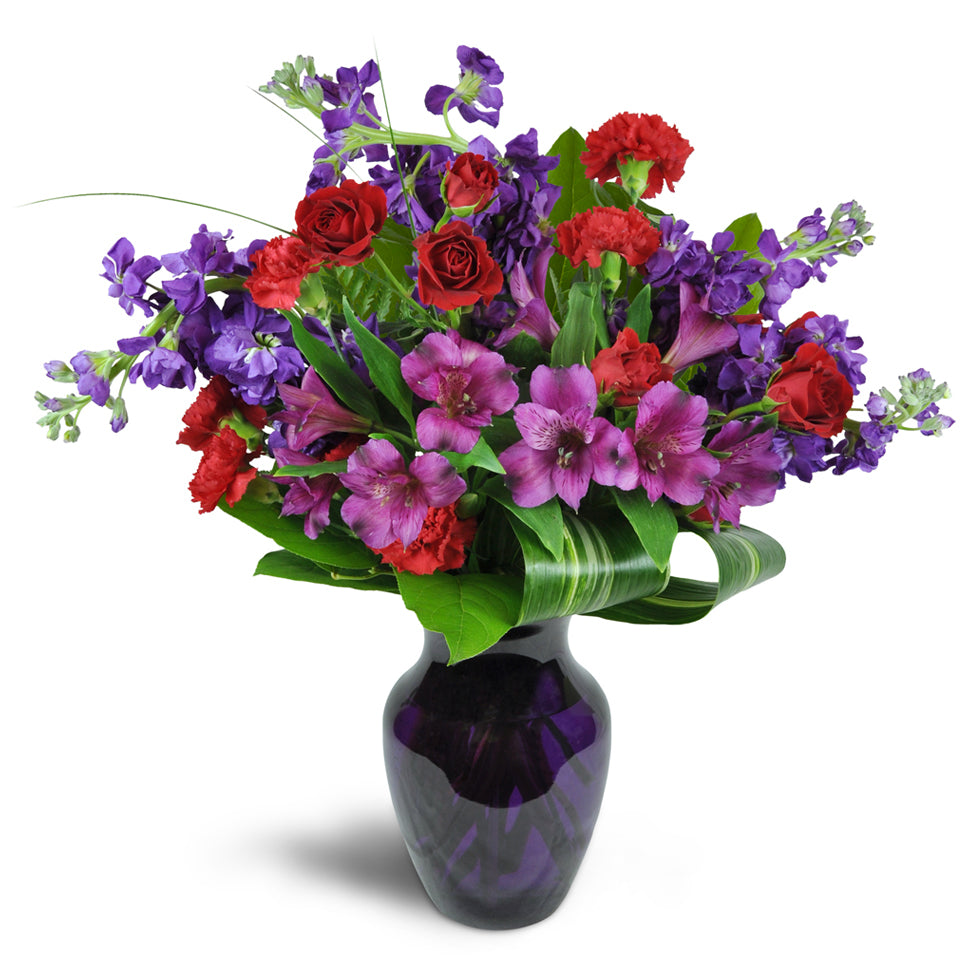 Romance Medley™ - Standard. Purple Peruvian lilies are arranged with stunning red spray roses and stock. Upgrade to Deluxe or Premium to add luxurious red roses.