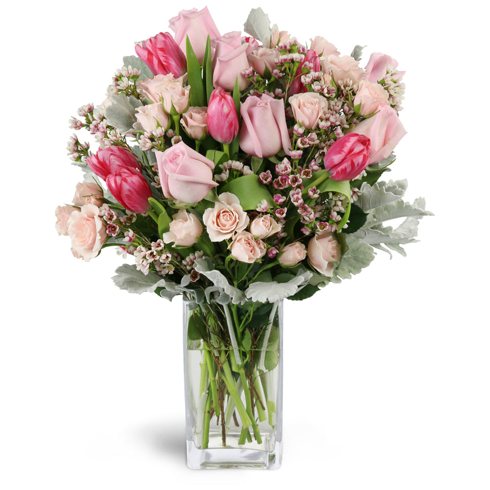 Sweetly Scented Pinks™ - Premium. Gift them an abundance of pink roses, spray roses, tulips, waxflower, and more arranged in a glass vase.