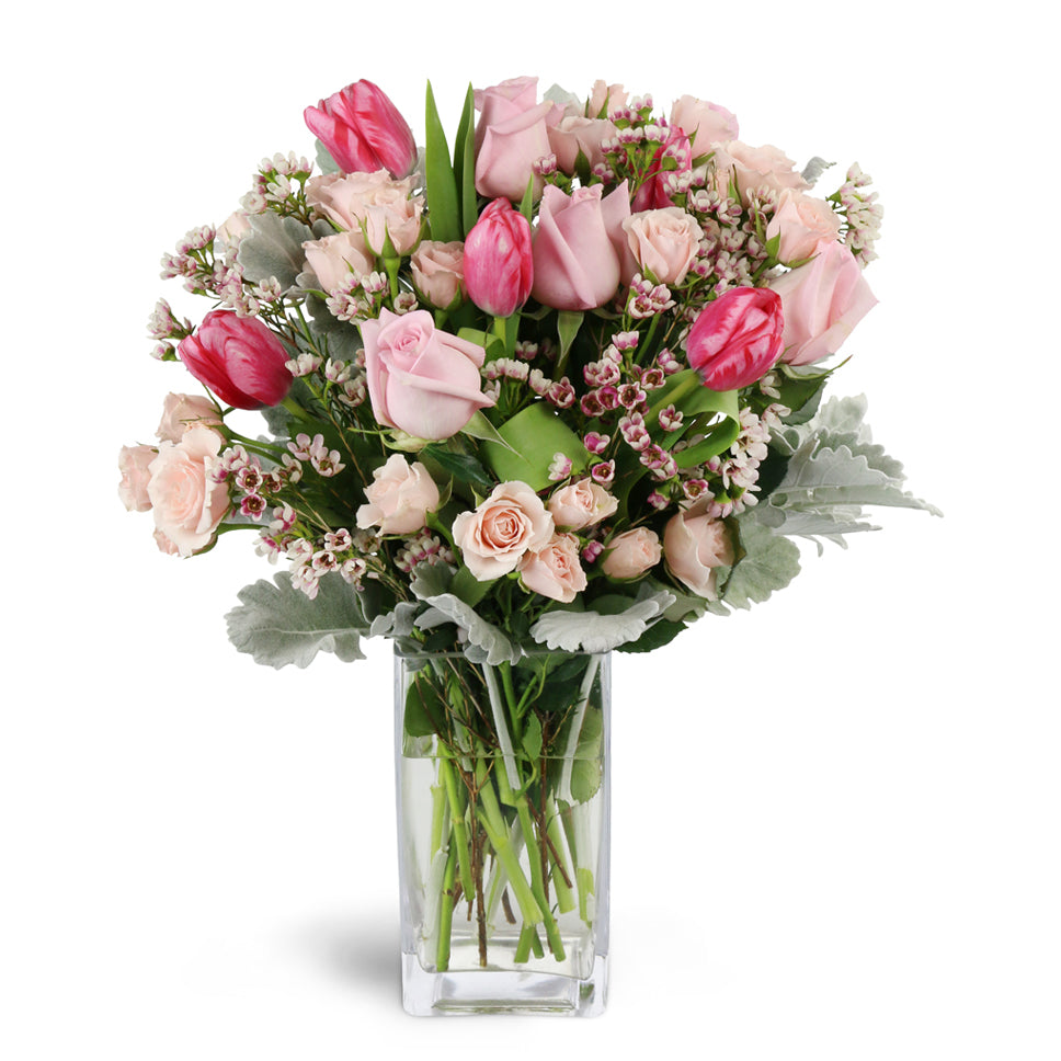 Sweetly Scented Pinks™ - Deluxe. Gift them an abundance of pink roses, spray roses, tulips, waxflower, and more arranged in a glass vase.