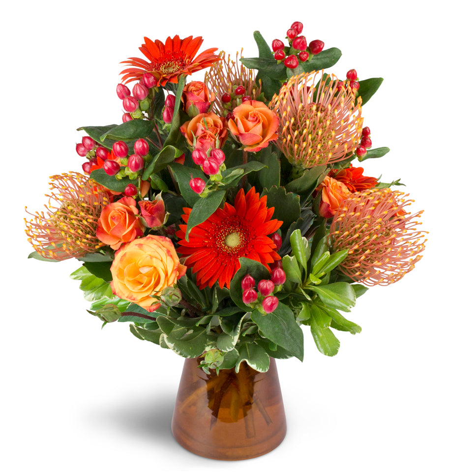 Energetic Orange™ - Deluxe. Unique pincushion protea are arranged with orange spray roses, mini Gerbera daisies, and more.