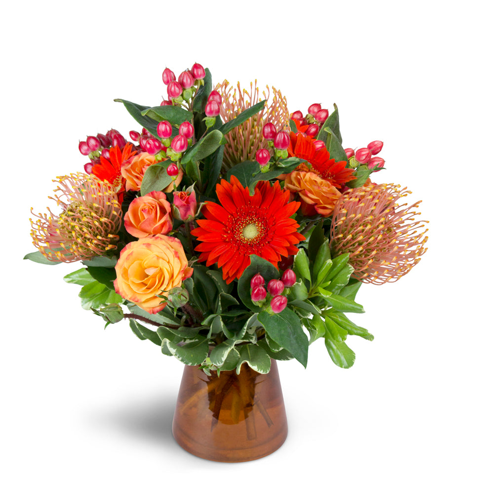 Energetic Orange™ - Standard. Unique pincushion protea are arranged with orange spray roses, mini Gerbera daisies, and more.