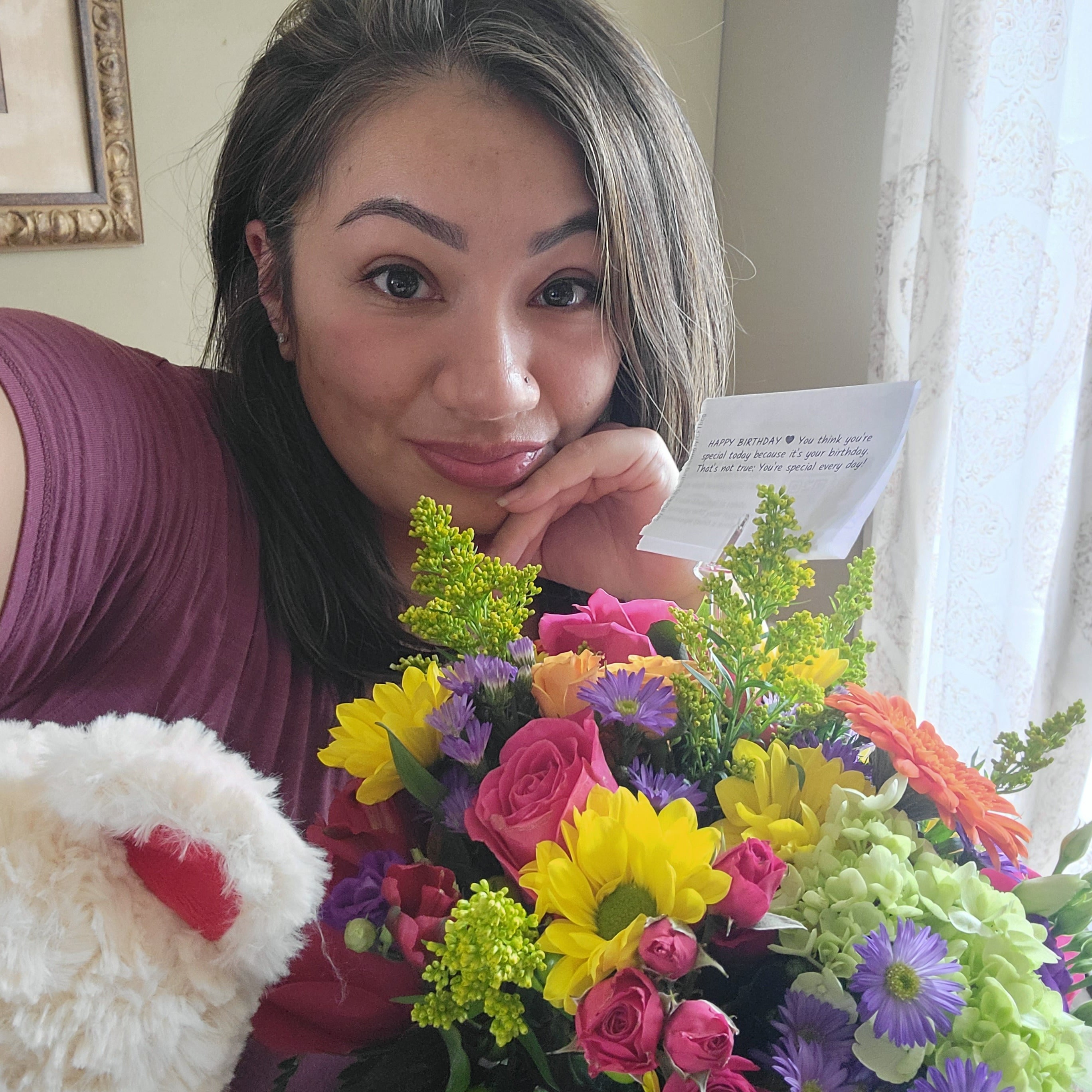 A heartfelt thanks for Birthday Blast. A woman smiling taking a selfie with her flowers next to a window with a white curtain.