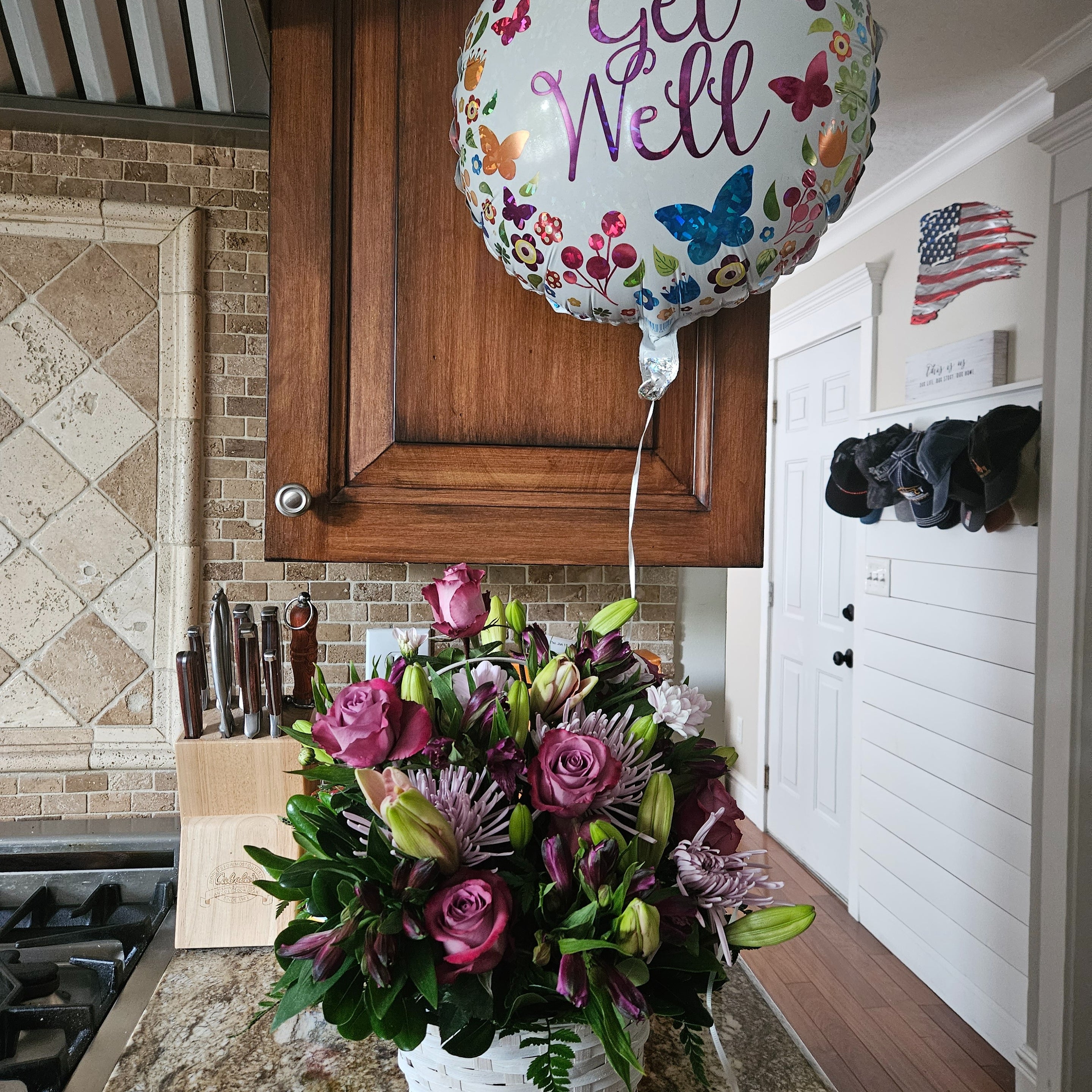 Recipient-submitted photo of Basket Full of Dreams floral arrangement in a white basket on a kitchen table with a Get Well Balloon.