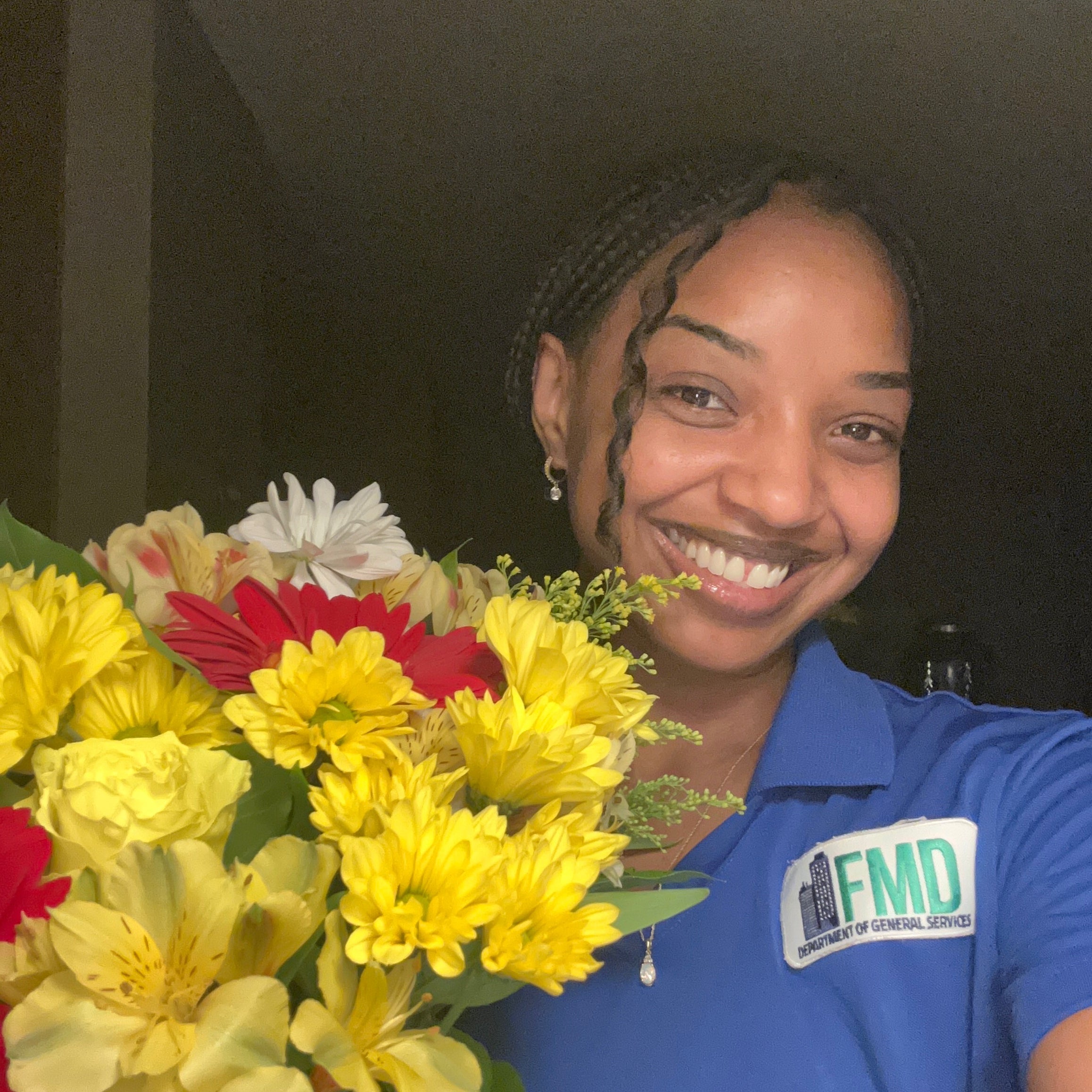 A heartfelt thanks for Bright Delight flowers. Woman smiling in a blue shirt holding the primarily yellow flower arrangement.