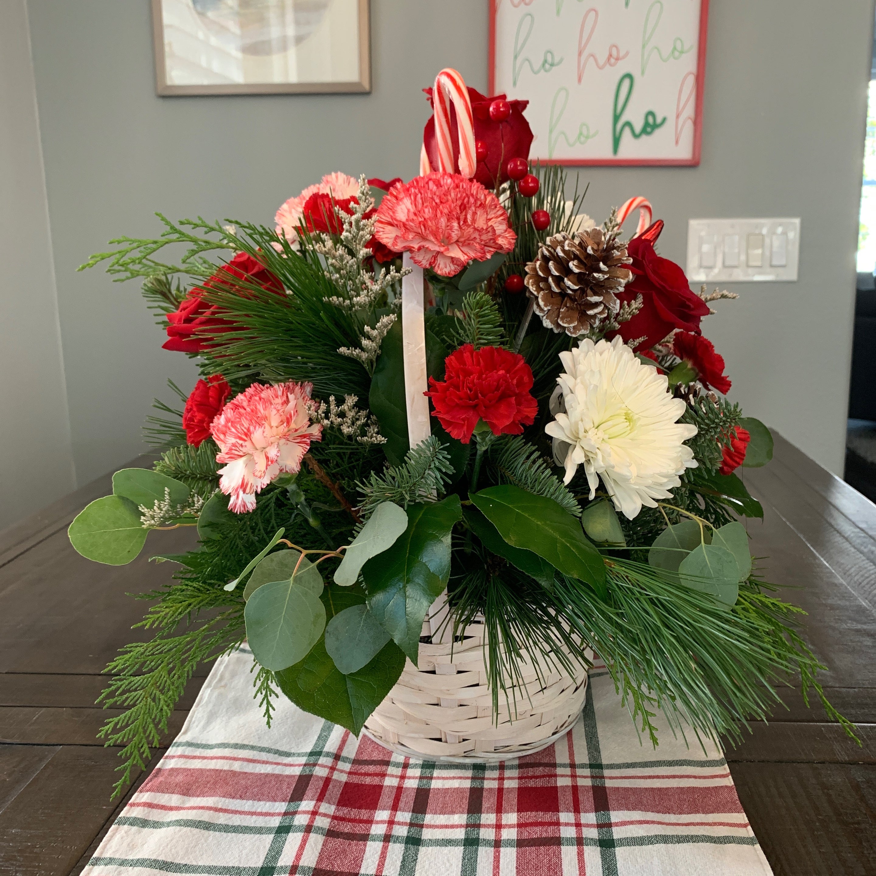 Recipient-submitted photo of Basket Full of Christmastime - floral arrangement in a basket. Red carnations, red mini Gerbera daisies, peppermint mini carnations, noble fir, cedar, and red ornament baubles are arranged in a classic woven basket.