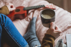 Cup of coffee held by person in bed