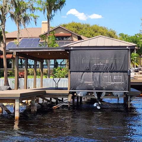 A mesh boathouse shade covers a tritoon boat on a boat lift, keeping it out of the sun
