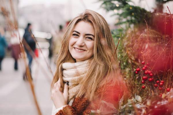 smiling woman stands in street next to festive foliage