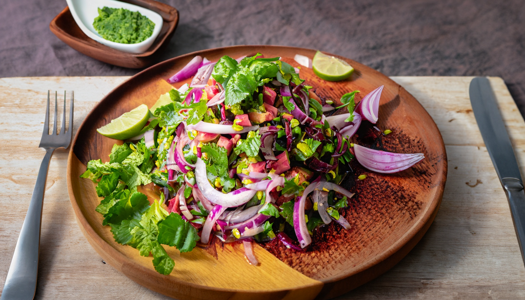 A fresh and colorful choko salad with thinly sliced choko, red onions, and cilantro, dressed with a tangy lime vinaigrette, served on a wooden platter with a fork and knife beside it