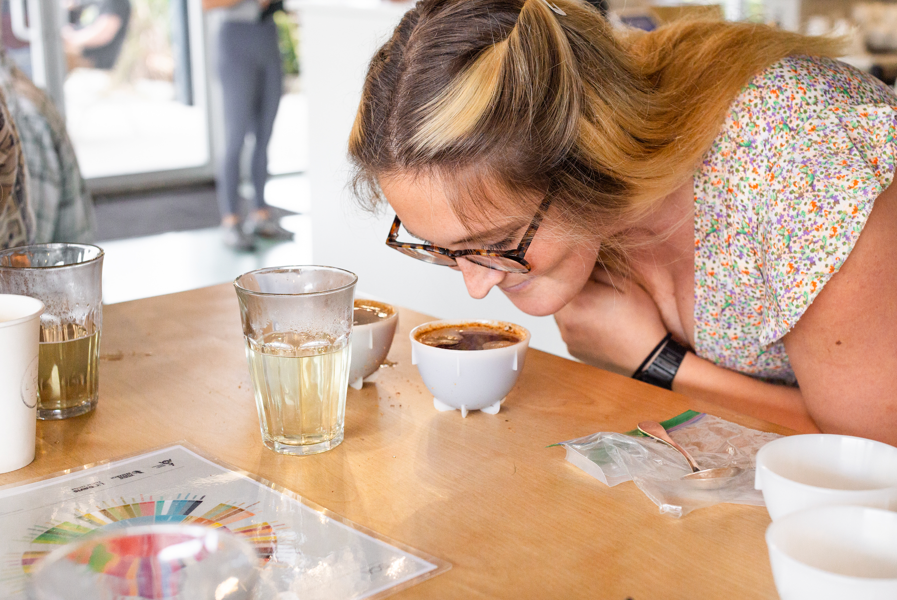 Woman leaning forward to smell a cup of coffee set on a table.