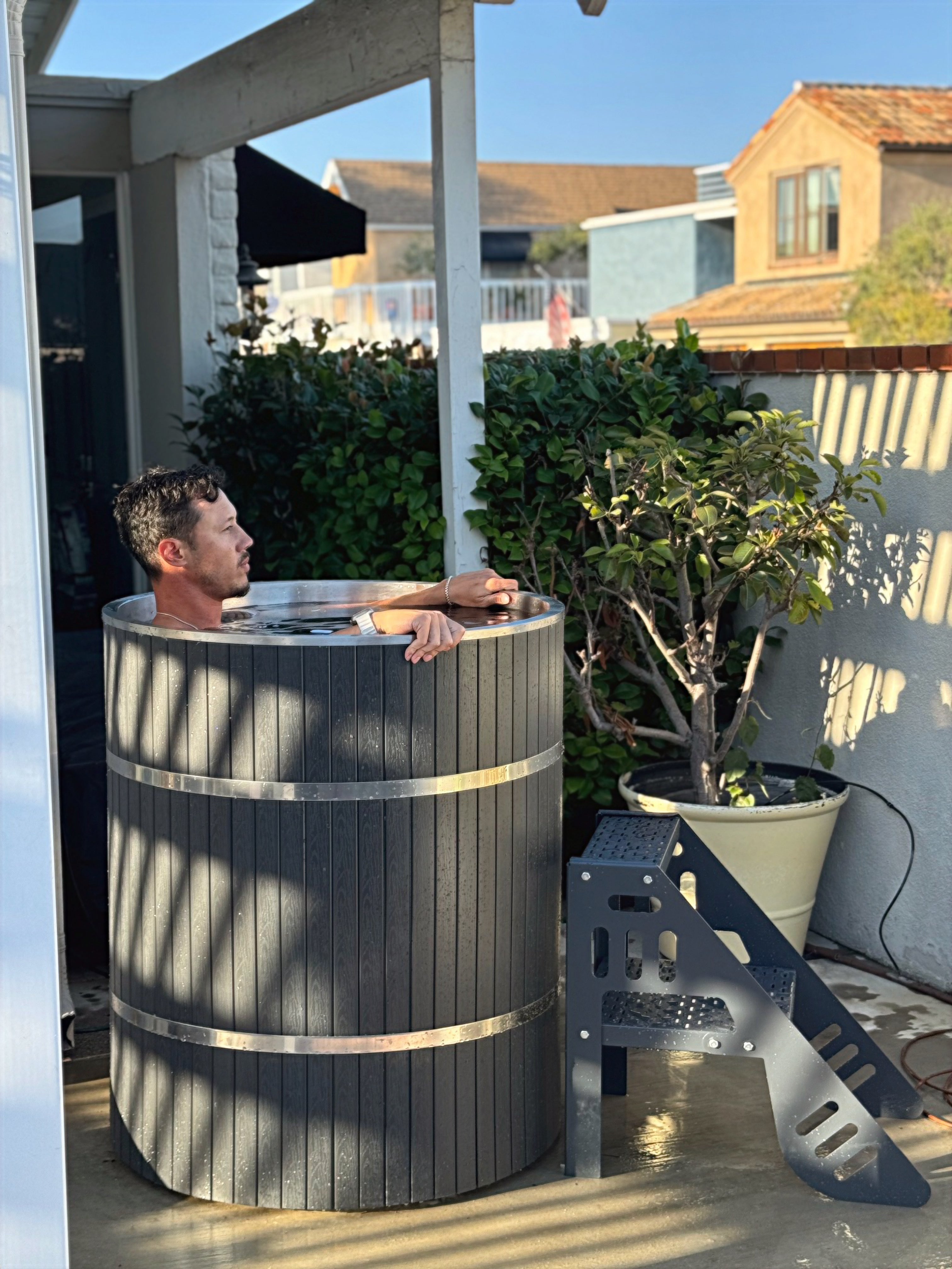 Outdoor hot tub with umbrellas, chairs, and a fire pit in a garden setting.