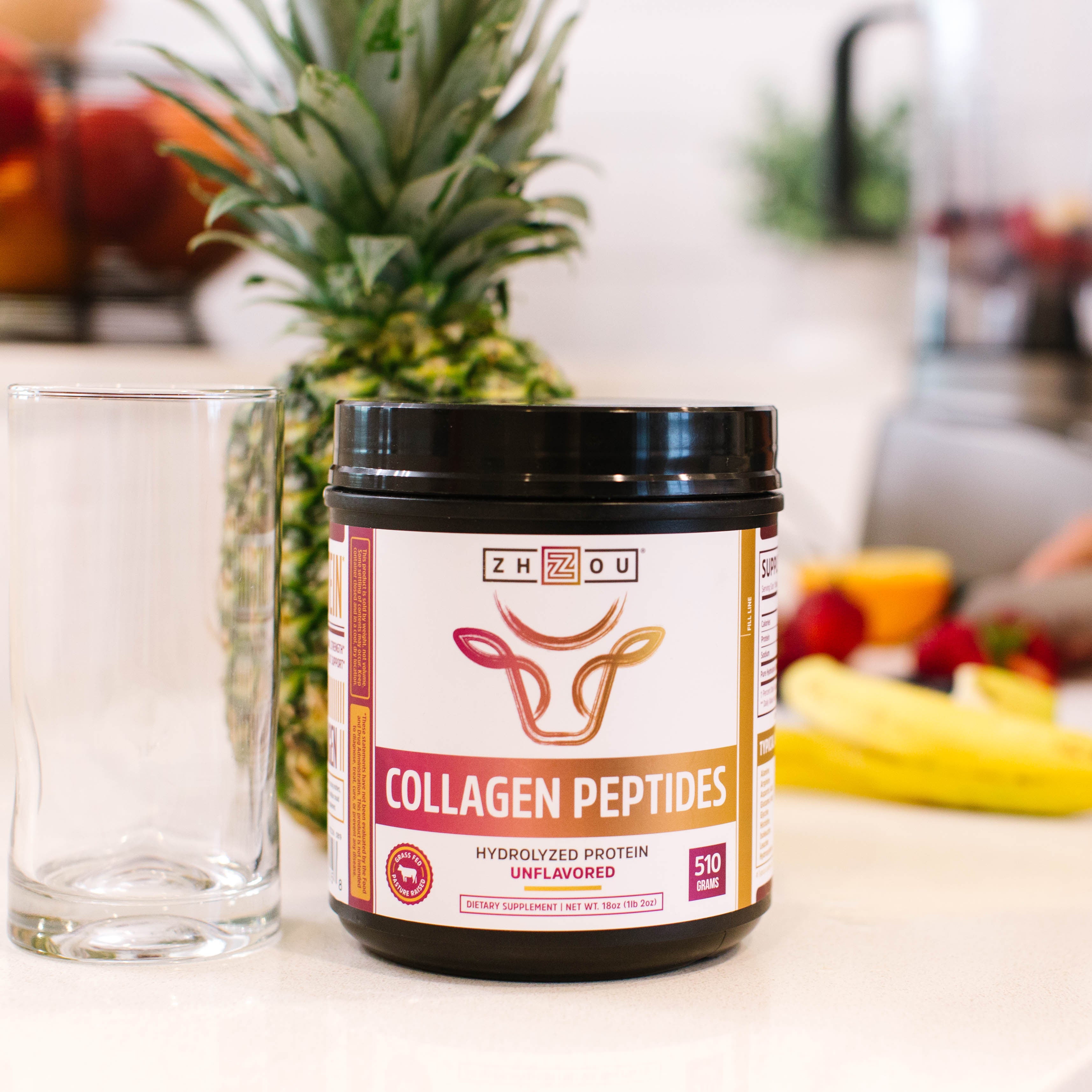 A tub of Zhou’s Collagen Peptides on a kitchen counter with pineapple and someone cooking in the background. 