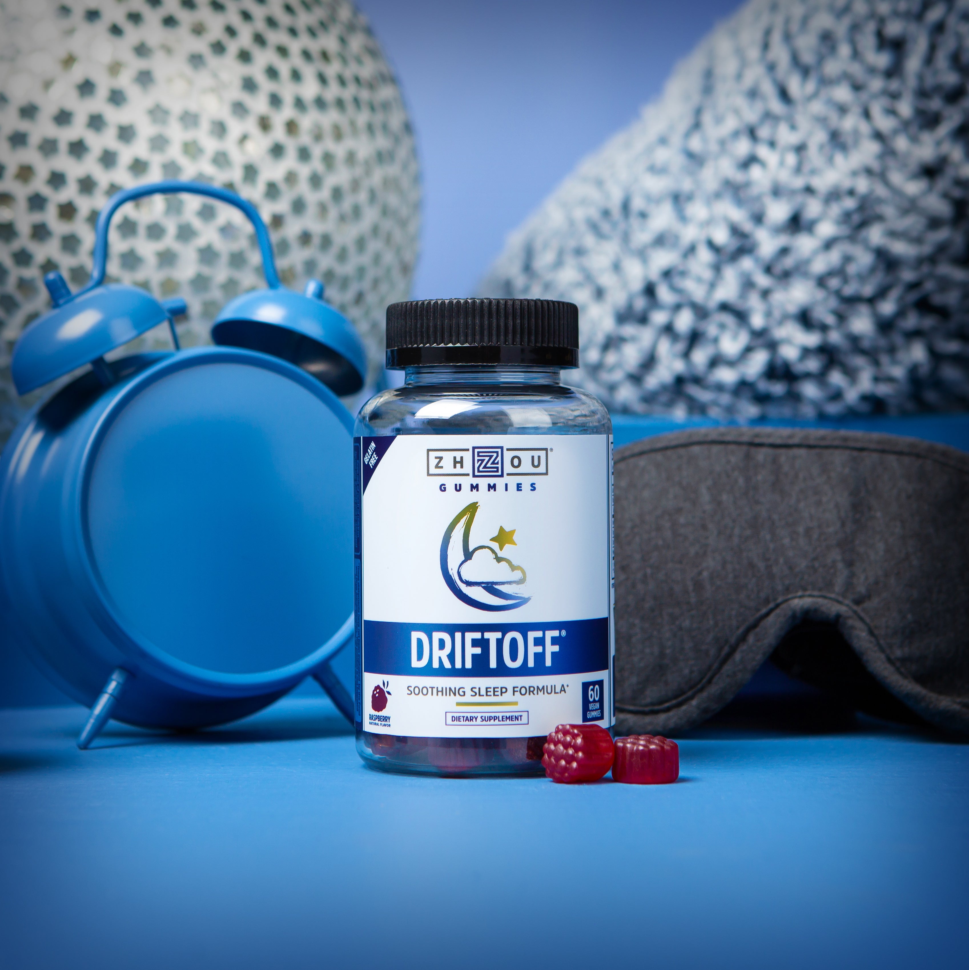 A bottle of Zhou Nutrition’s Driftoff gummies, with a blue background, an alarm clock and a sleeping mask.