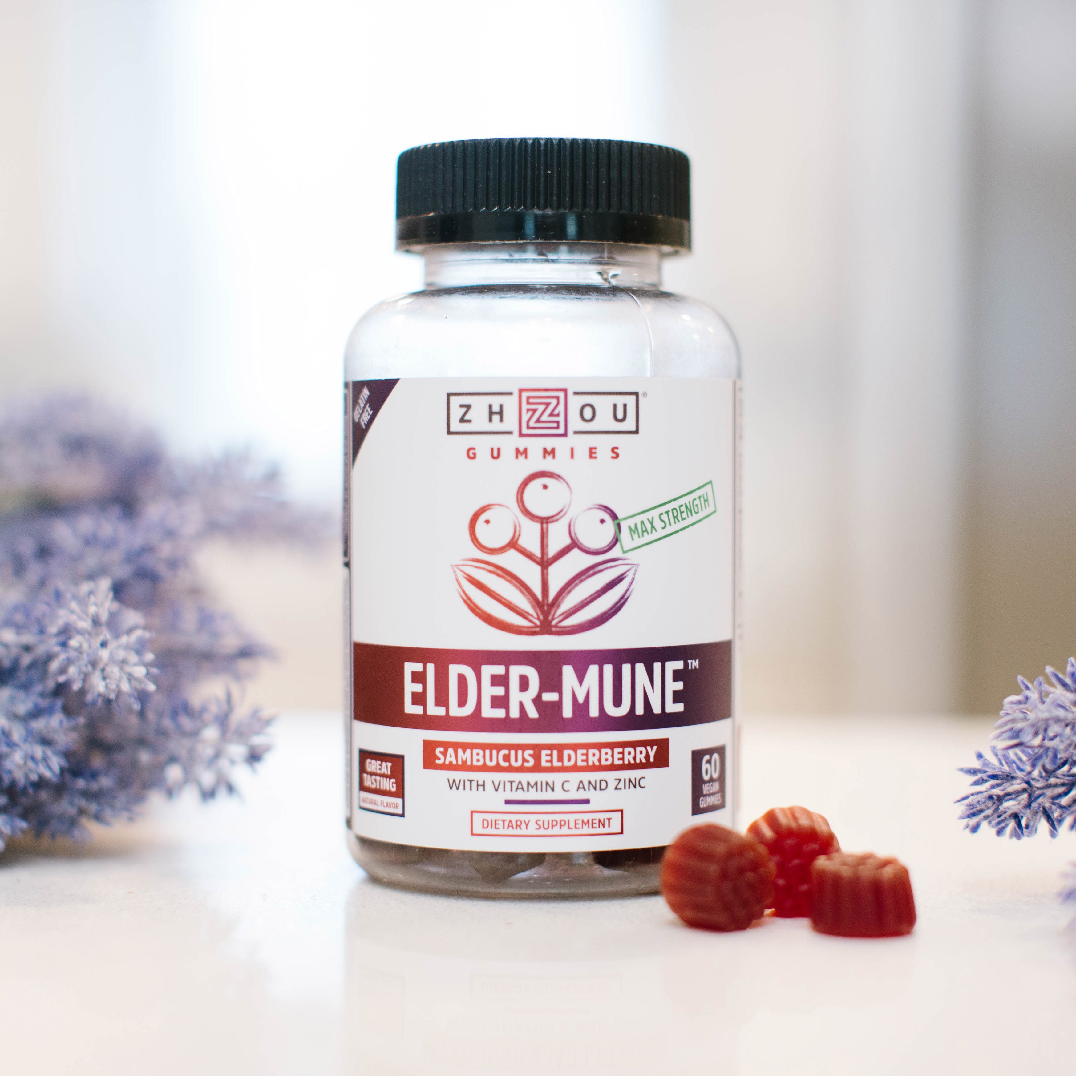 A bottle of Zhou’s Elder-Mune gummies on a white counter with purple flowers surrounding it.
