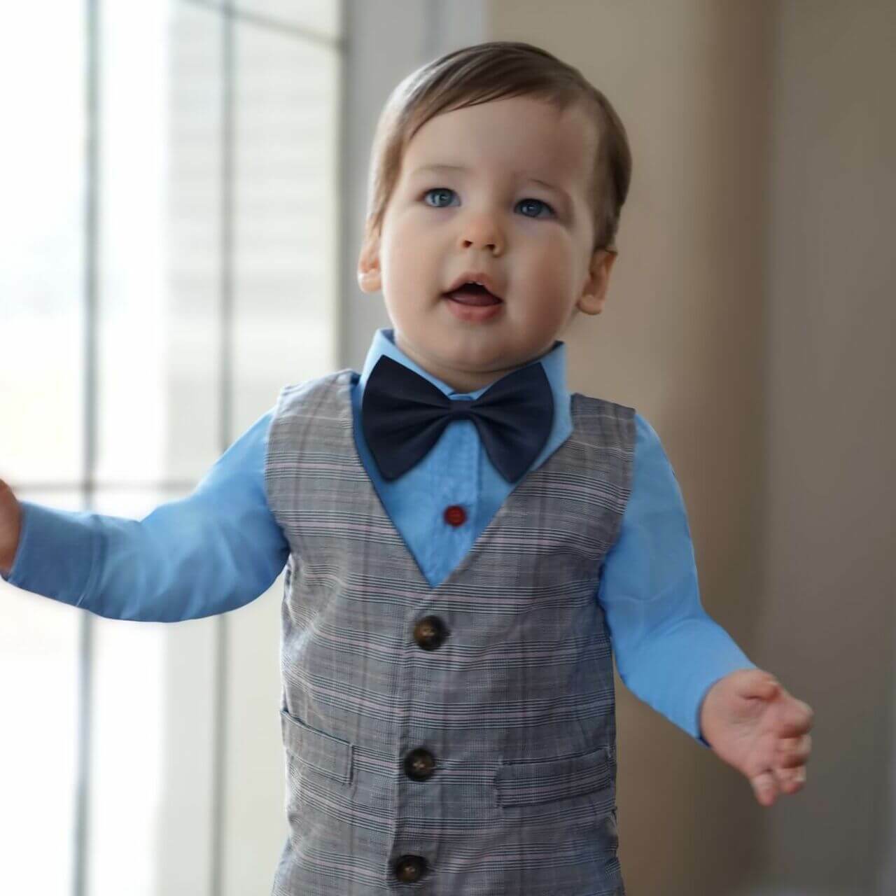 Toddler in blue shirt and plaid vest with bowtie