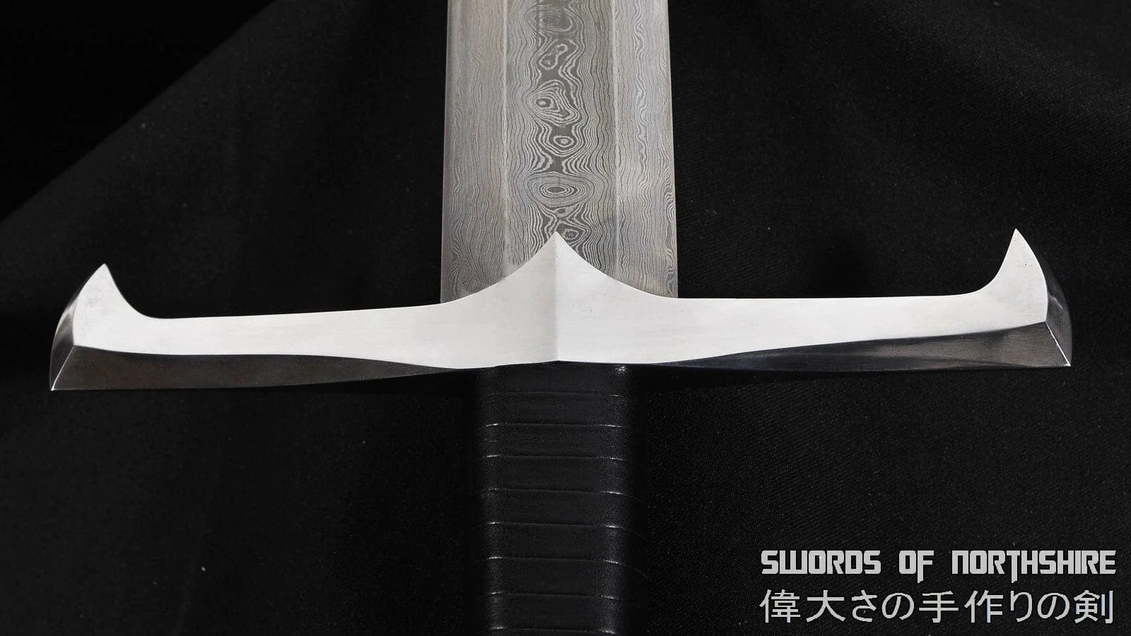 close-up of the silver blade, blade pattern, and guard of a European longsword on a black background