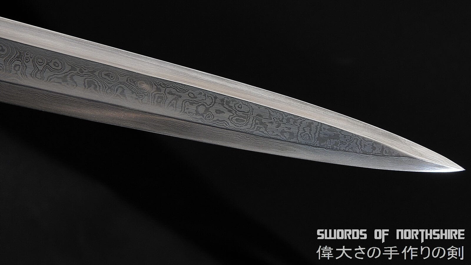 close-up of the silver blade, blade pattern, and tip of a European longsword on a black background