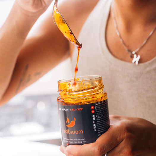 Person holding spoon dripping chili crisp over an open jar.