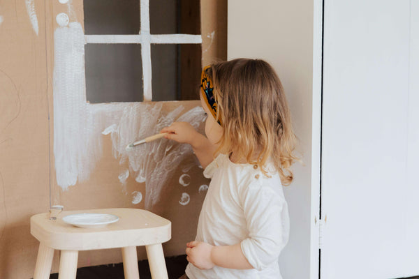 Criança a pintar uma estrutura de papel semelhante a uma casa.