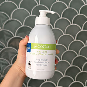 MooGoo Cream Conditioner in hand against a wall