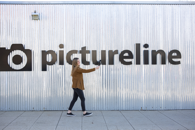 vlogger using a tripod grip to take video in front of pictureline sign