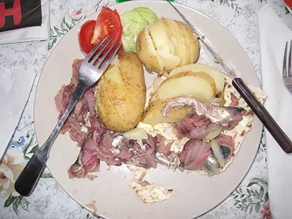 a plate with Surströmming and baked potato, tomato, and onions