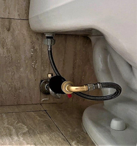 Bloc d'eau mécanique installé sur une toilette dans un plan horizontal. Le bloc d'eau est doté de raccords pour se connecter à une vanne d'arrêt d'eau et à un tuyau d'alimentation. Il s'agit d'un dispositif de sécurité qui peut être utilisé pour arrêter l'écoulement de l'eau vers les toilettes en cas de fuite ou autre problème.