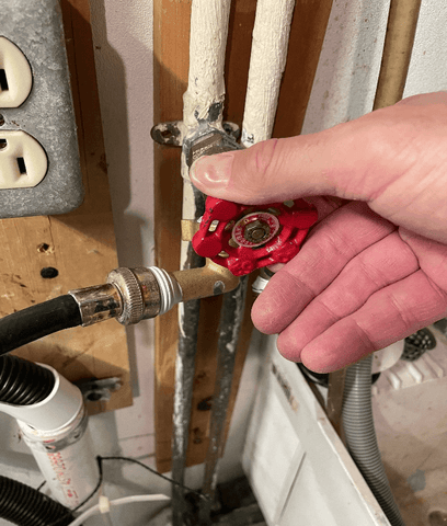 Hand turning off a hot water supply valve. Shutting off the water feed to the washing machine.