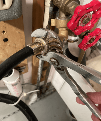 Loosening a hose connected to a valve with a wrench. Washing machine hose is tightened onto the supply valve.