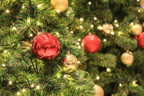 A close-up of a fake Christmas tree with red and gold baubles and lights