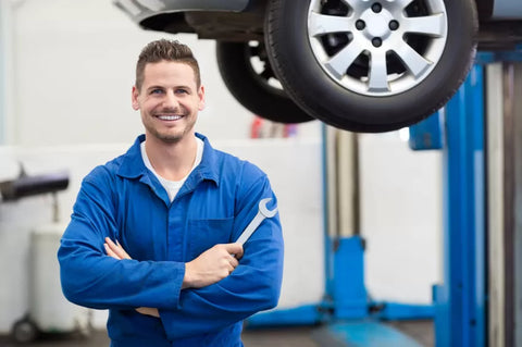 A professional automotive mechanic who is smiling and holding a spanner.