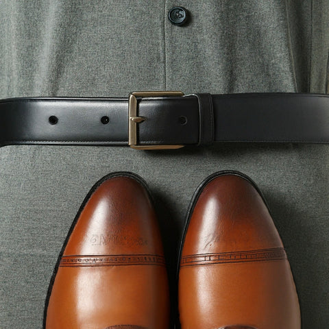 Black dress belt cinched around contrasting brown leather shoes.