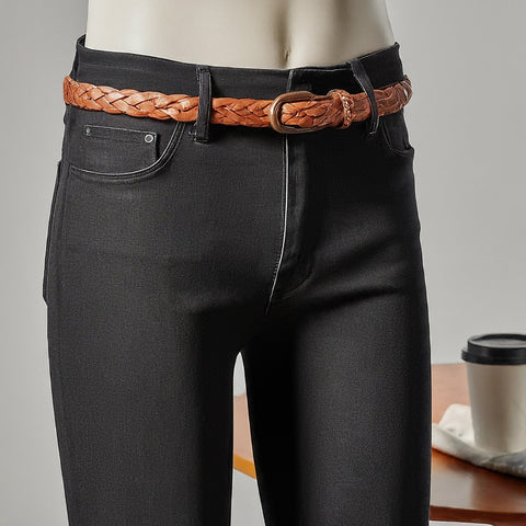 A close-up view of black jeans on a mannequin, featuring a brown woven leather belt resting on the belt loops.
